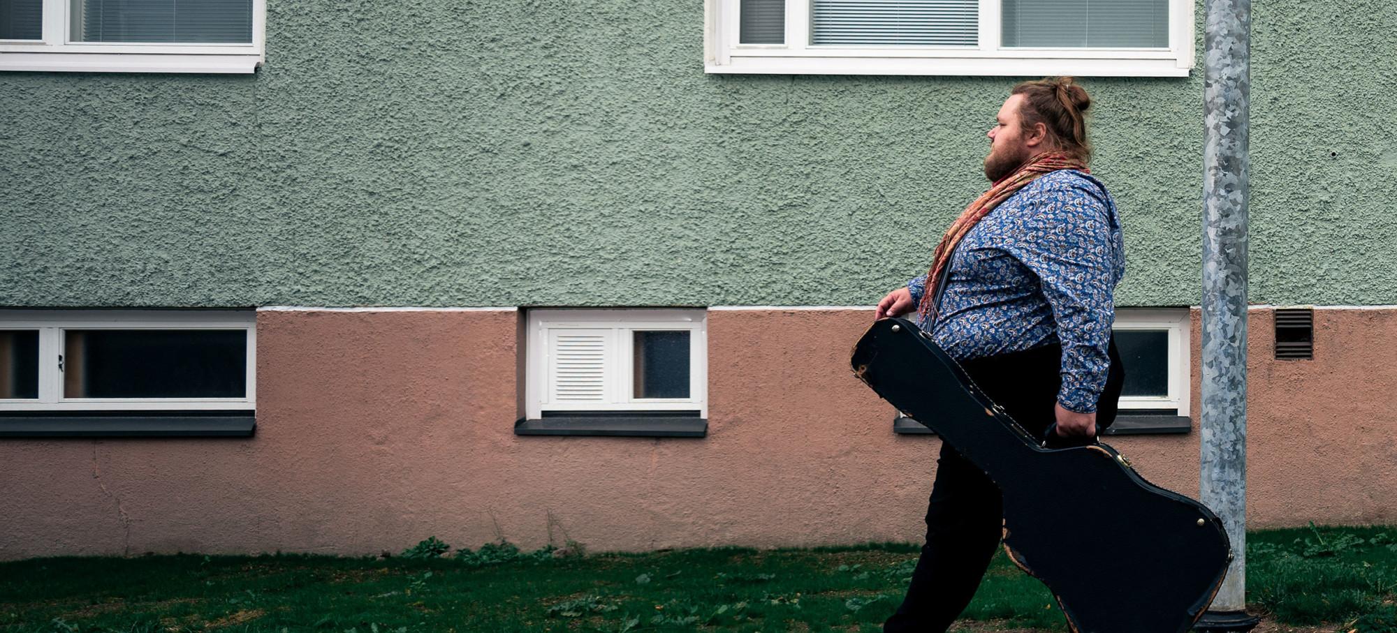 A man walks down the street with a guitar case.